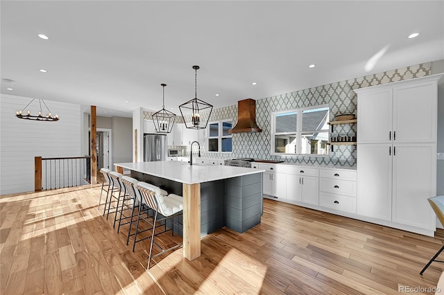 kitchen with white cabinetry, hanging light fixtures, a kitchen breakfast bar, a kitchen island with sink, and custom exhaust hood