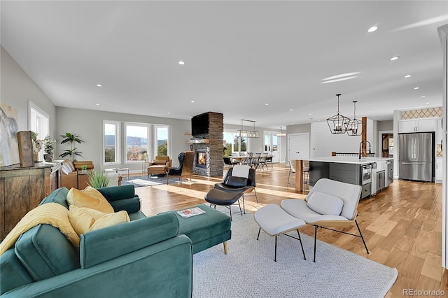 living room featuring light hardwood / wood-style flooring, a stone fireplace, a healthy amount of sunlight, and a notable chandelier