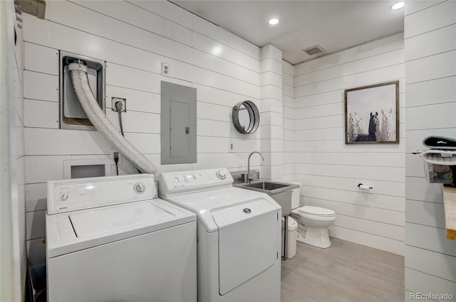 laundry room featuring wooden walls, sink, electric panel, and washing machine and clothes dryer