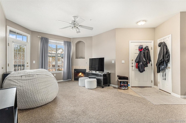 interior space featuring baseboards, ceiling fan, light carpet, a tiled fireplace, and access to outside