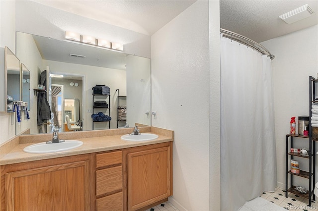 bathroom with double vanity, visible vents, a textured ceiling, and a sink