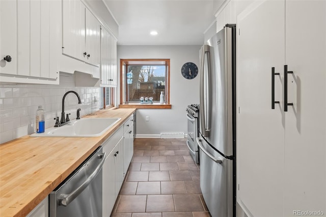 kitchen with dark tile patterned floors, sink, tasteful backsplash, appliances with stainless steel finishes, and white cabinets