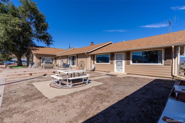 back of property with a patio, a shingled roof, and a chimney