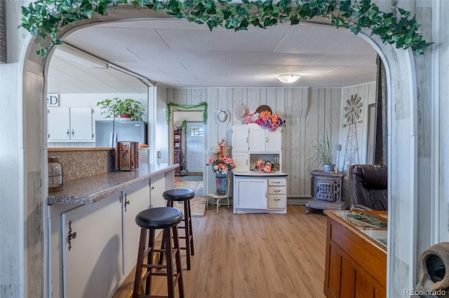 kitchen featuring light wood finished floors, arched walkways, white cabinets, and freestanding refrigerator