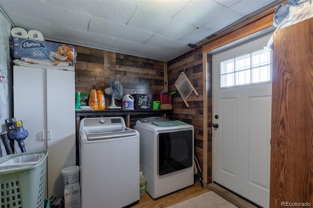 clothes washing area with washer and dryer, cabinet space, wood walls, and light wood finished floors