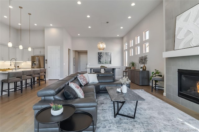 living area with recessed lighting, light wood-style floors, a high ceiling, and a tile fireplace