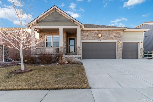 view of front of home with a front yard, driveway, covered porch, stone siding, and a garage