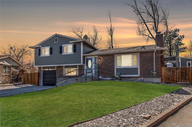 split level home featuring a lawn, a chimney, aphalt driveway, fence, and brick siding