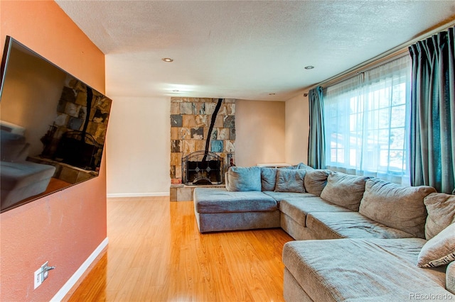 living area with light wood-type flooring, a wood stove, a textured ceiling, and baseboards