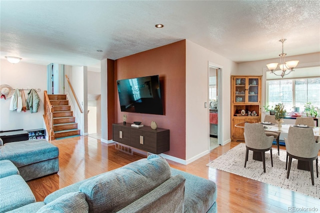 living area with a textured ceiling, a notable chandelier, baseboards, stairs, and light wood-type flooring