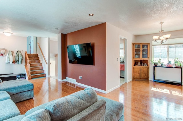 living area featuring light wood finished floors, stairway, an inviting chandelier, a textured ceiling, and baseboards