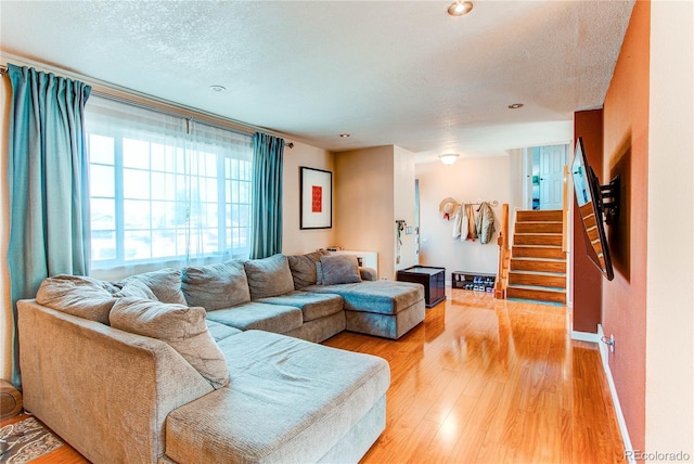 living room featuring stairs, a textured ceiling, baseboards, and light wood-style floors