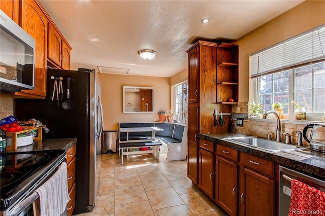 kitchen featuring brown cabinets, stainless steel appliances, backsplash, light tile patterned flooring, and a sink