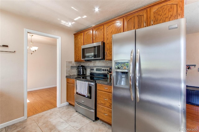 kitchen with dark countertops, stainless steel appliances, light tile patterned flooring, and brown cabinets