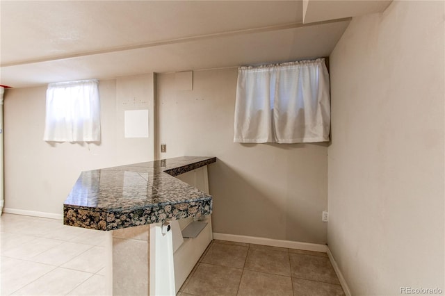 kitchen with light tile patterned floors, a peninsula, baseboards, and tile countertops