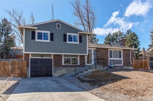 split level home with driveway, a chimney, an attached garage, fence, and brick siding