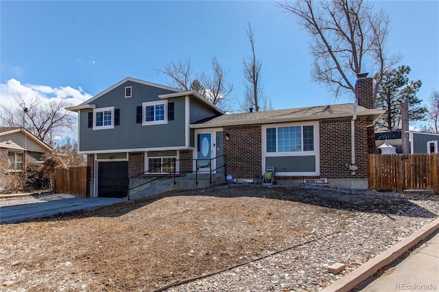 tri-level home with brick siding, a chimney, an attached garage, fence, and driveway