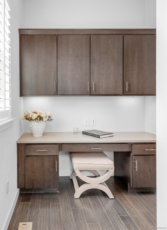 unfurnished office featuring built in desk, dark wood-type flooring, and baseboards