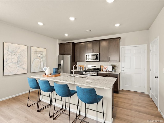 20802 E 66th Ave, Aurora, CO 80019 - kitchen featuring stainless steel appliances, an island with sink, a kitchen bar, light wood-type flooring, and recessed lighting