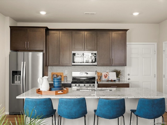 20802 E 66th Ave, Aurora, CO 80019 - kitchen featuring appliances with stainless steel finishes, dark brown cabinetry, light stone countertops, a kitchen bar, and recessed lighting
