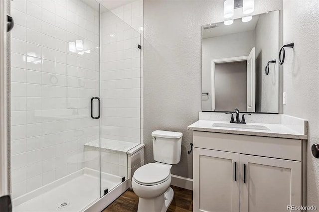 bathroom with a textured wall, toilet, wood finished floors, vanity, and a shower stall