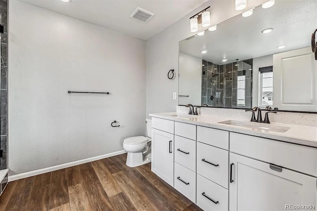 bathroom featuring wood finished floors, a sink, visible vents, double vanity, and a stall shower