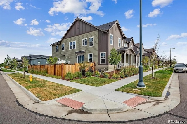 view of property featuring board and batten siding, a front yard, fence, and a residential view