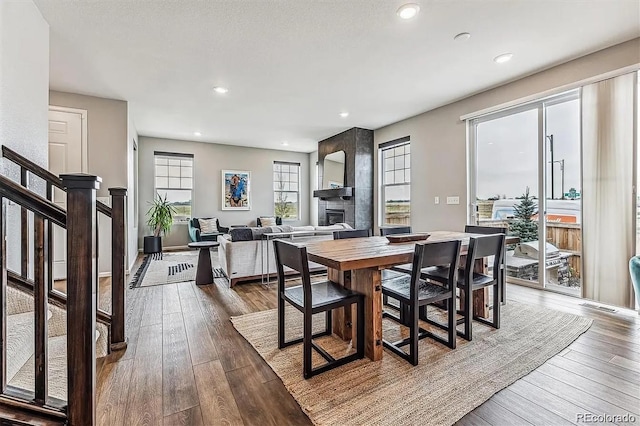 dining area with a large fireplace, stairway, dark wood finished floors, and recessed lighting