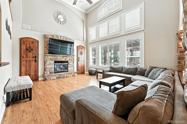 7809 S Coolidge Way, Aurora, CO 80016 - living room featuring a high ceiling, ornamental molding, a ceiling fan, a stone fireplace, and light wood finished floors