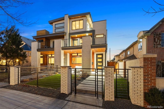 modern home featuring brick siding, a fenced front yard, a gate, and a balcony