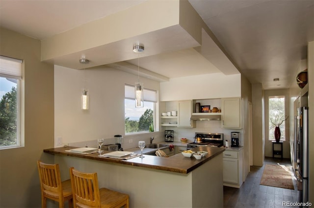 kitchen featuring kitchen peninsula, decorative light fixtures, dark wood-type flooring, appliances with stainless steel finishes, and a kitchen breakfast bar