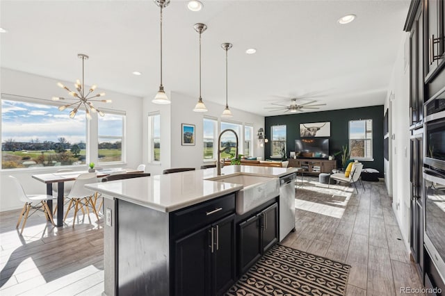 kitchen with sink, light hardwood / wood-style flooring, appliances with stainless steel finishes, pendant lighting, and a kitchen island with sink