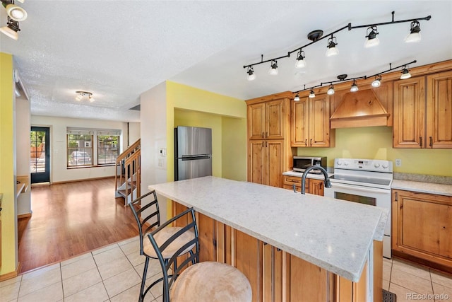 1209 S Flower Cir Unit C, Lakewood, CO 80232 - kitchen featuring stainless steel appliances, custom range hood, light tile patterned flooring, an island with sink, and light stone countertops