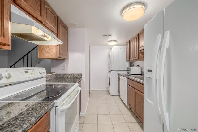 kitchen featuring light tile patterned flooring, white appliances, stacked washer / dryer, and dark stone counters