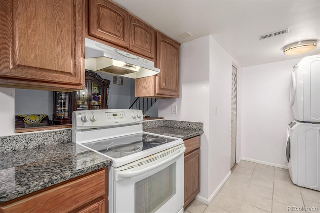 kitchen with light tile patterned floors, electric range, dark stone counters, and stacked washer / drying machine