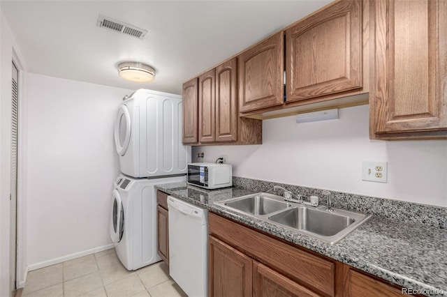 kitchen featuring white appliances, sink, light tile patterned floors, stacked washer and clothes dryer, and dark stone countertops