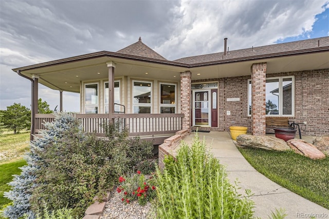 view of front of property featuring brick siding, covered porch, and roof with shingles