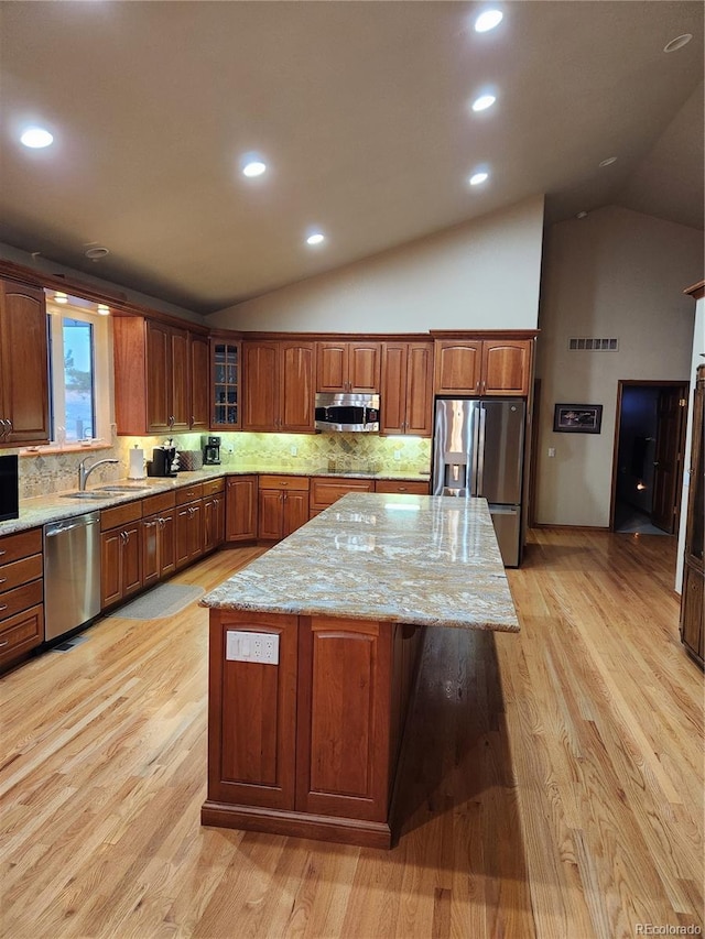 kitchen featuring lofted ceiling, a center island, stainless steel appliances, light wood finished floors, and light stone countertops