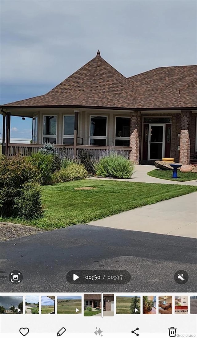 view of front of house featuring brick siding, a front yard, and roof with shingles