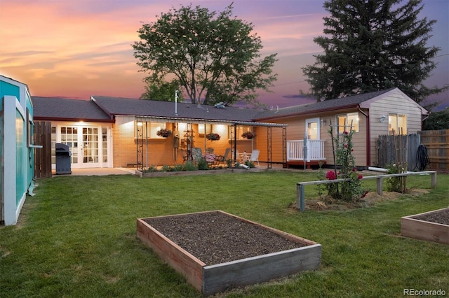 back house at dusk with french doors and a lawn