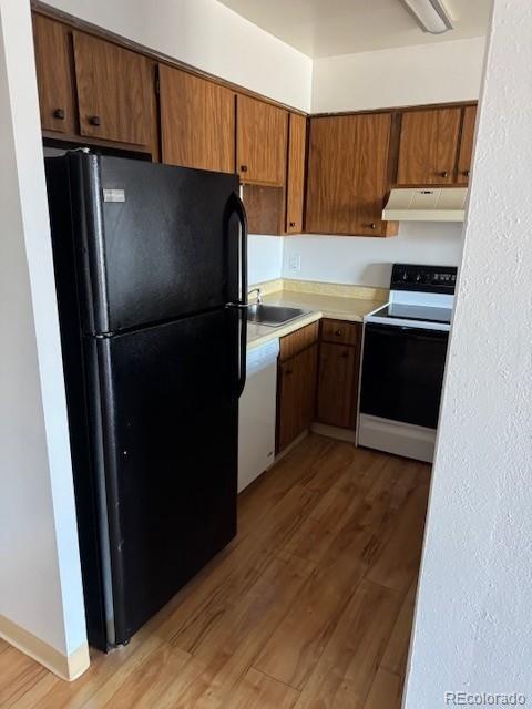 kitchen with freestanding refrigerator, white dishwasher, light wood-type flooring, under cabinet range hood, and range with electric stovetop