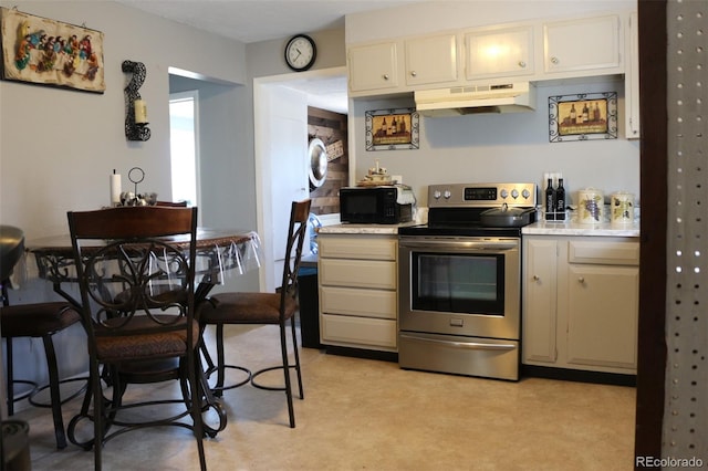 kitchen with cream cabinetry, stacked washing maching and dryer, and stainless steel electric range oven