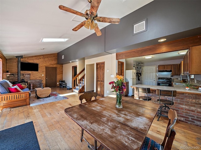 10852 Conifer Mountain Rd, Conifer, CO 80433 - dining room featuring light wood-style floors, ceiling fan, stairs, a wood stove, and wood walls