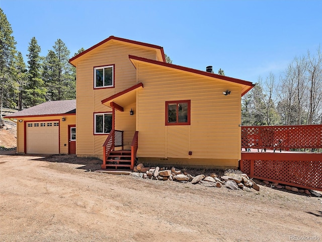 10852 Conifer Mountain Rd, Conifer, CO 80433 - view of front facade with a garage, dirt driveway, roof with shingles, and a wooden deck