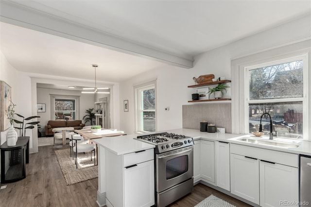 kitchen with a peninsula, a sink, light countertops, appliances with stainless steel finishes, and hanging light fixtures