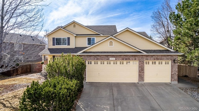 traditional-style house with a garage, brick siding, concrete driveway, and fence