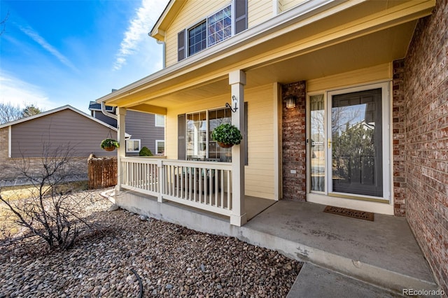 view of exterior entry with brick siding and a porch