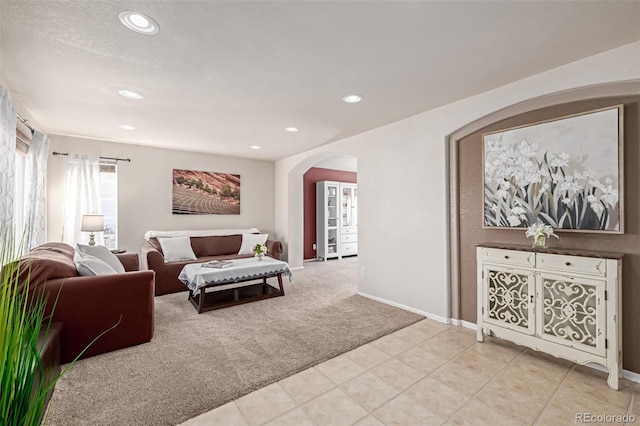 living room with baseboards, light tile patterned flooring, recessed lighting, arched walkways, and light carpet