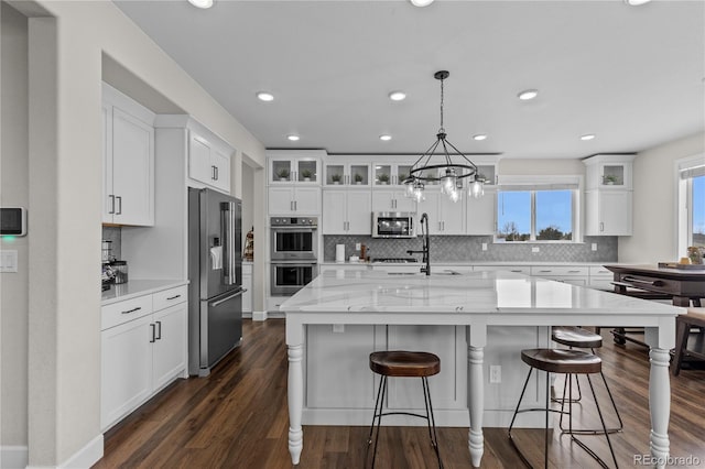 kitchen with a kitchen island with sink, white cabinetry, pendant lighting, and appliances with stainless steel finishes