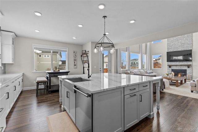 kitchen featuring dishwasher, decorative light fixtures, a stone fireplace, light stone countertops, and a kitchen island with sink